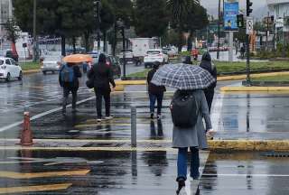 Las personas, que caminan por el sector de La Carolina, en Quito, usan ropa abrigada y paraguas para protegerse de la lluvia.