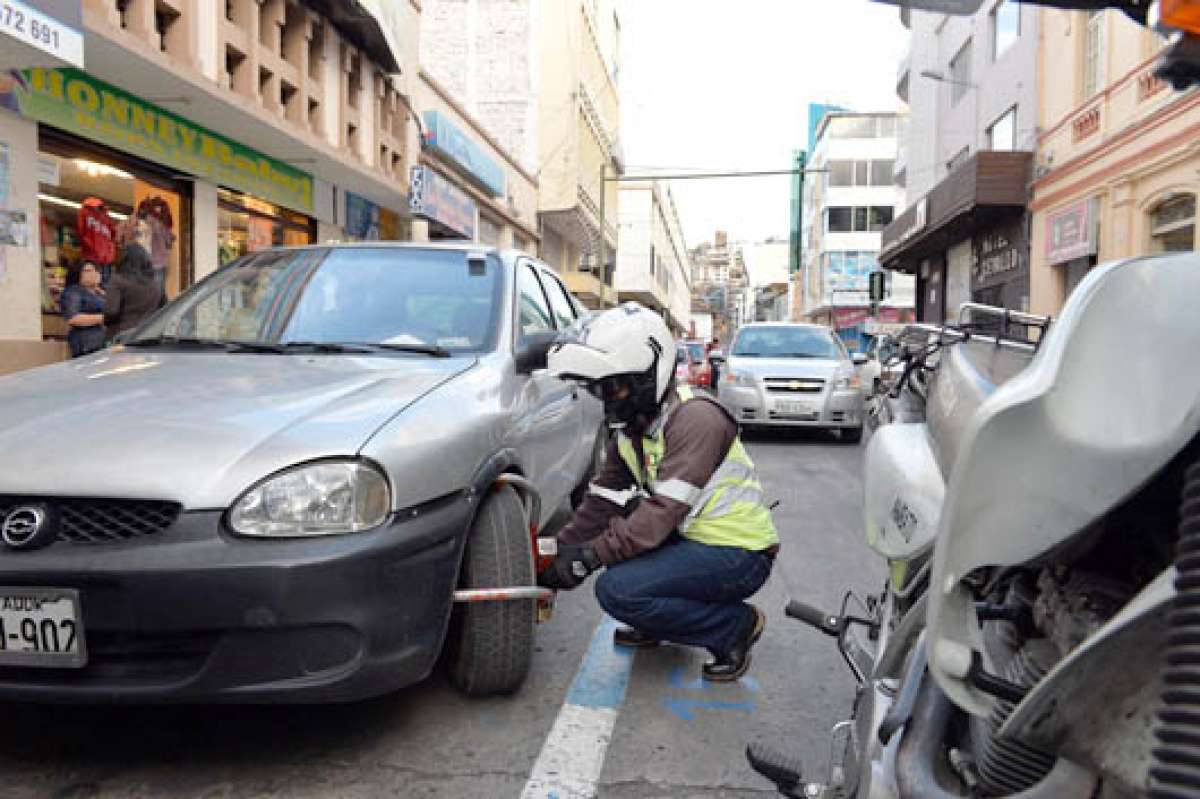 Personal del Simert coloca el candado de inmovilizaci&oacute;n a un veh&iacute;culo que excedi&oacute; su tiempo de parqueo en una calle c&eacute;ntrica. Foto: Roberto Ch&aacute;vez