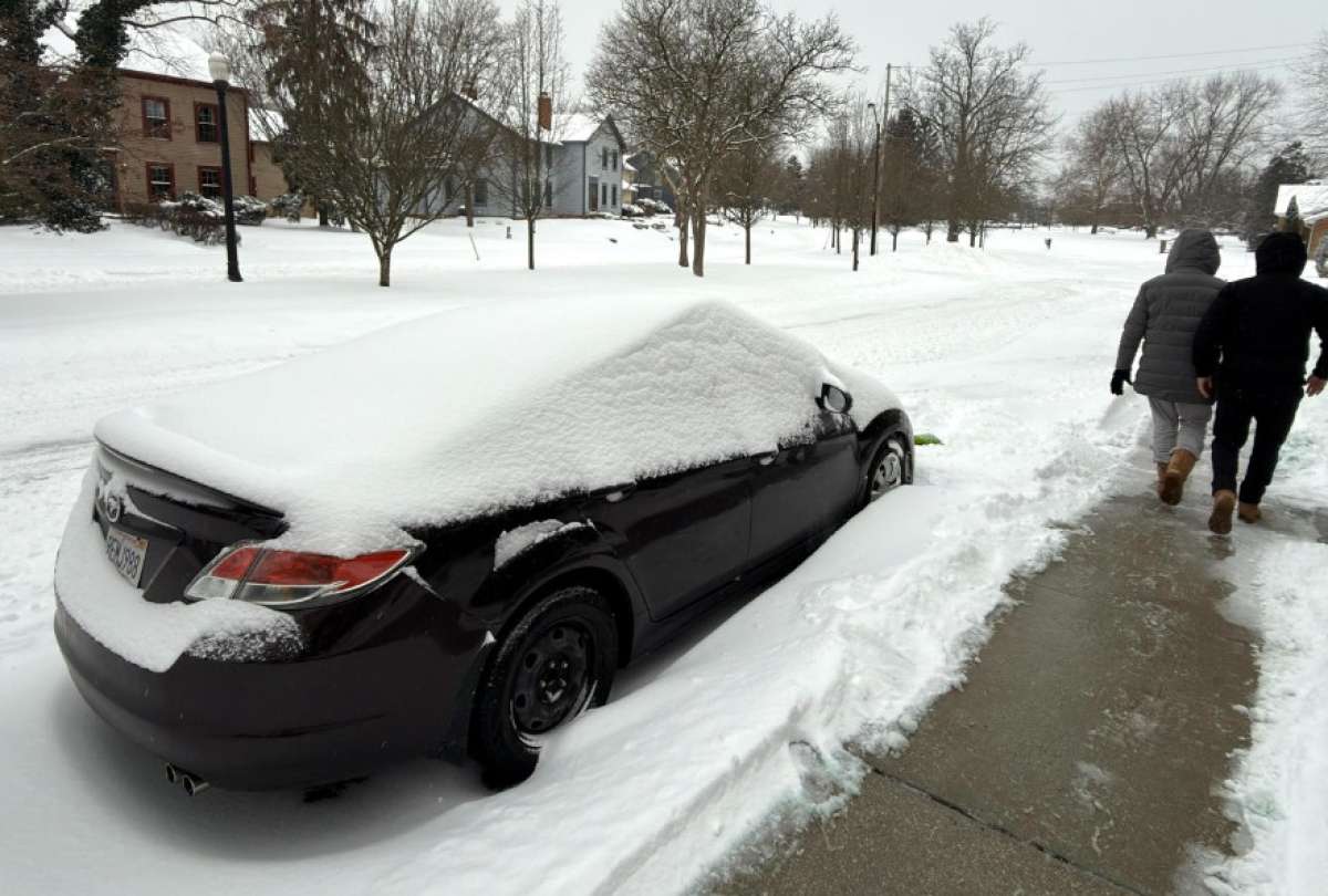 Dos personas caminan al lado de una calle afectada por la nieve este domingo en la ciudad de Hudson, Ohio (EE.UU.).