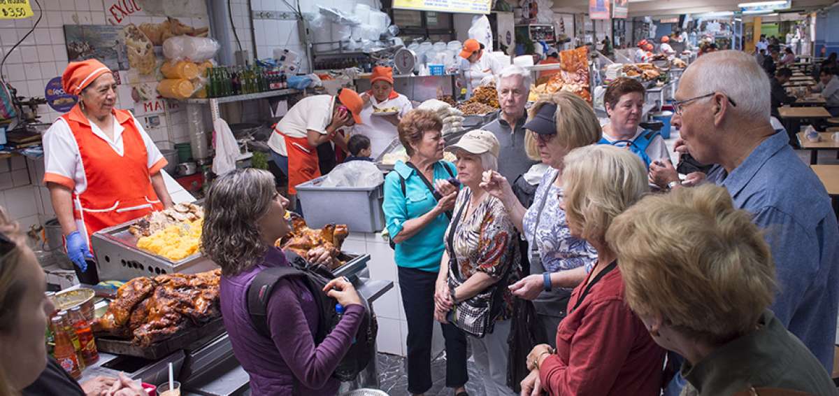Una gu&iacute;a tur&iacute;stica explica a un grupo de turistas sobre la preparaci&oacute;n del hornado en el mercado La Carolina.