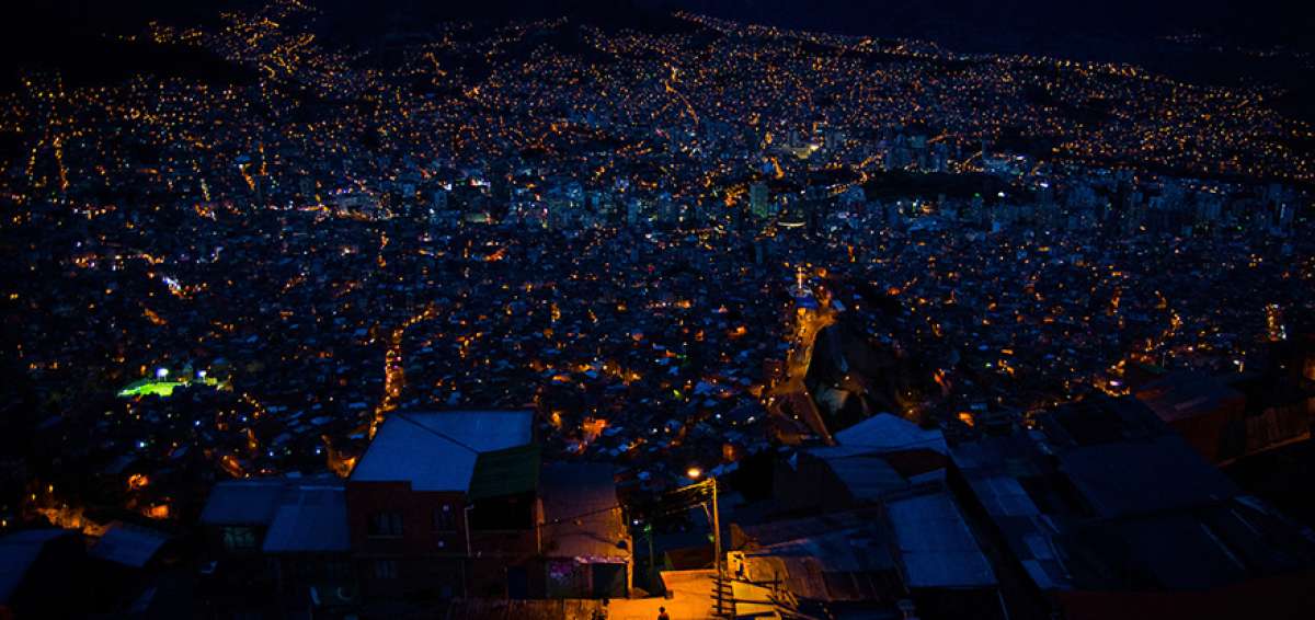 En la imagen se observa a un hombre caminando solo por la noche en El Alto, iluminado por la luz amarilla de la ciudad. &Eacute;l transita por la calle de los Yatitris.