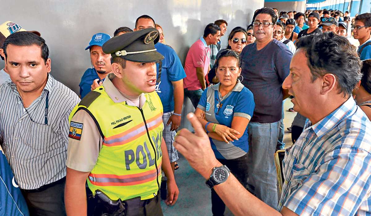 Un polic&iacute;a le explica a un socio que las entradas se estaban imprimiendo y que tenga paciencia. Al menos eso le dijeron al uniformado los representantes del club. Foto: Lylibeth Coloma / El Tel&eacute;grafo.