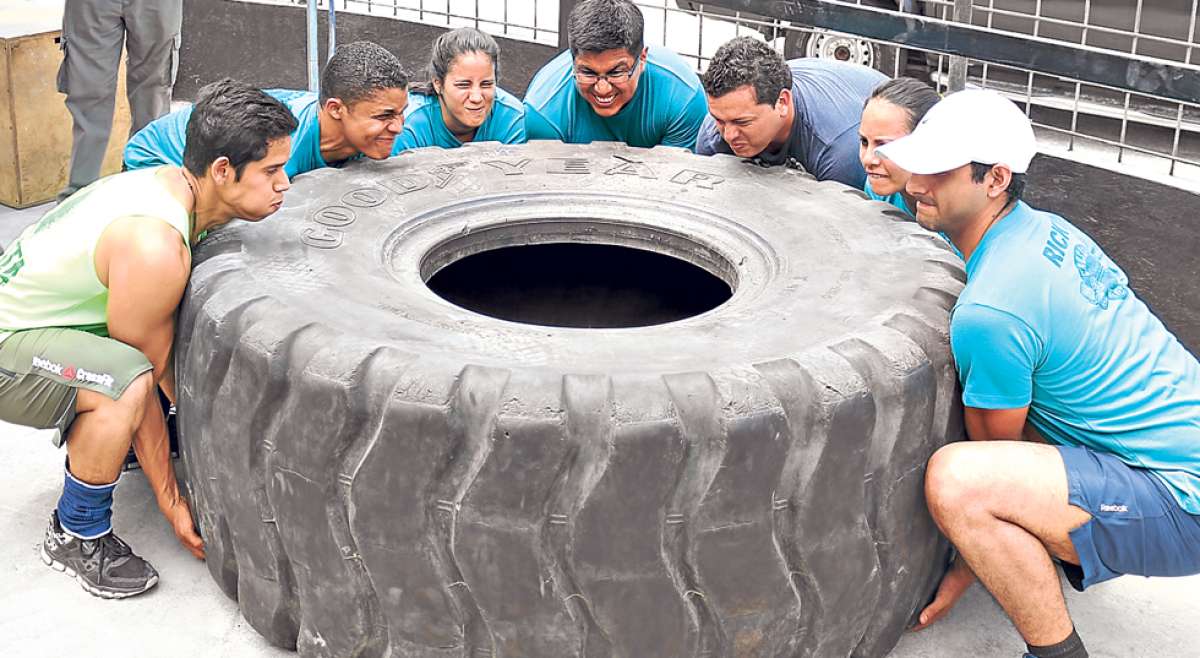 Varios atletas trabajan grupalmente para conseguir un objetivo com&uacute;n. En la foto se observa c&oacute;mo 7 de ellos intentan levantar una llanta. Foto: cortes&iacute;a