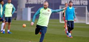 Andr&eacute;s Iniesta ejecuta un tiro libre durante un entrenamiento del FC Barcelona. Messi y Su&aacute;rez lo observan atr&aacute;s. 