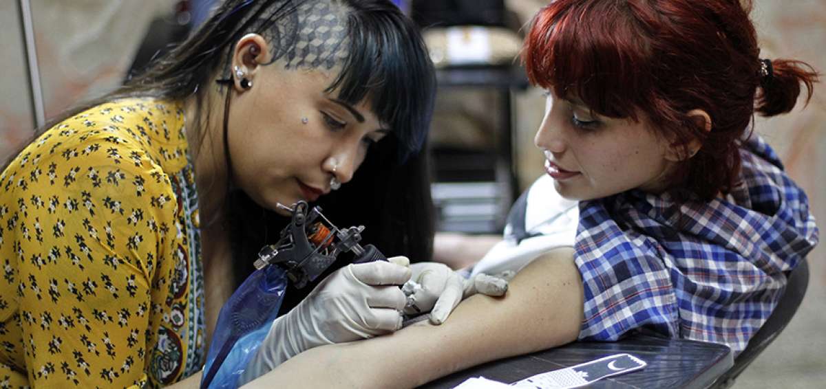La cantante de la banda de rock Los Locos Tristes, Zammys, observa su tatuaje realizado por Ana Lyem Lara (a la izquierda), profesional cubana.