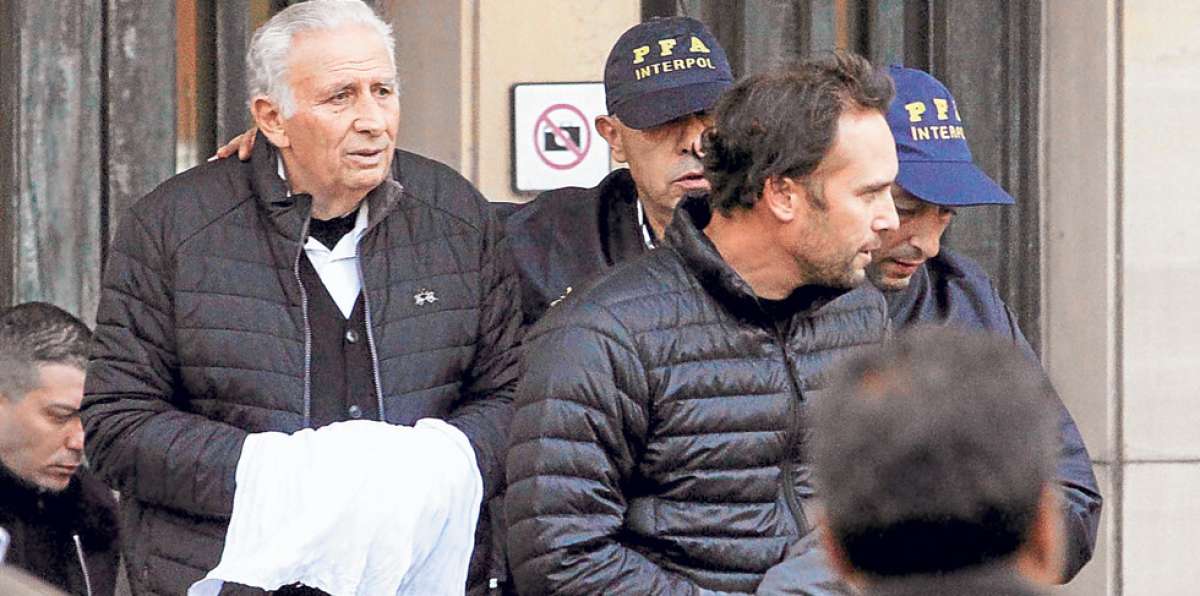 Escondiendo con ropa las esposas en sus mu&ntilde;ecas, Hugo (i) y Mariano Jinkis son llevados por la Interpol. Foto: internet
