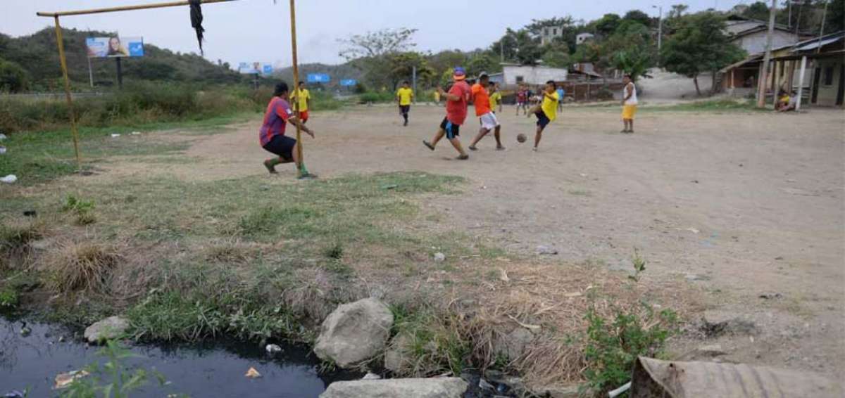Los j&oacute;venes en El Consuelo terminan el d&iacute;a jugando f&uacute;tbol en una pedregosa cancha, adecentada con su esfuerzo. A cada minuto, el bal&oacute;n termina en un canal de aguas servidas. Foto al lado: las condiciones en que vive la poblaci&oacute;n.