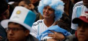 En Buenos Aires, una aficionada argentina llora la eliminaci&oacute;n de la Albiceleste mientras sostiene a un beb&eacute; entre sus brazos.