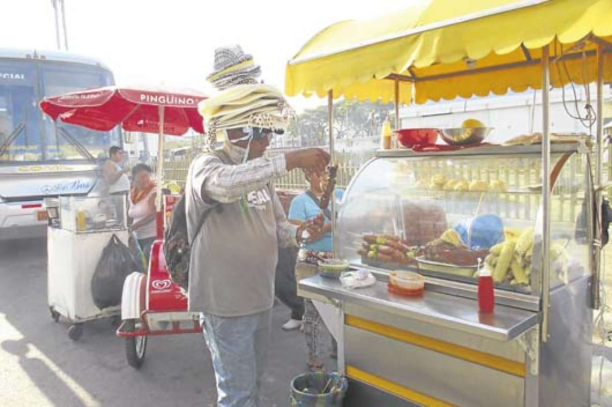 Cerca al paso Guayaquil-Santay 8 (sur) se comercializan alimentos. Un vendedor de sombreros consume uno de los productos que se vende en carretilla.  Foto: Ronny Paredes.