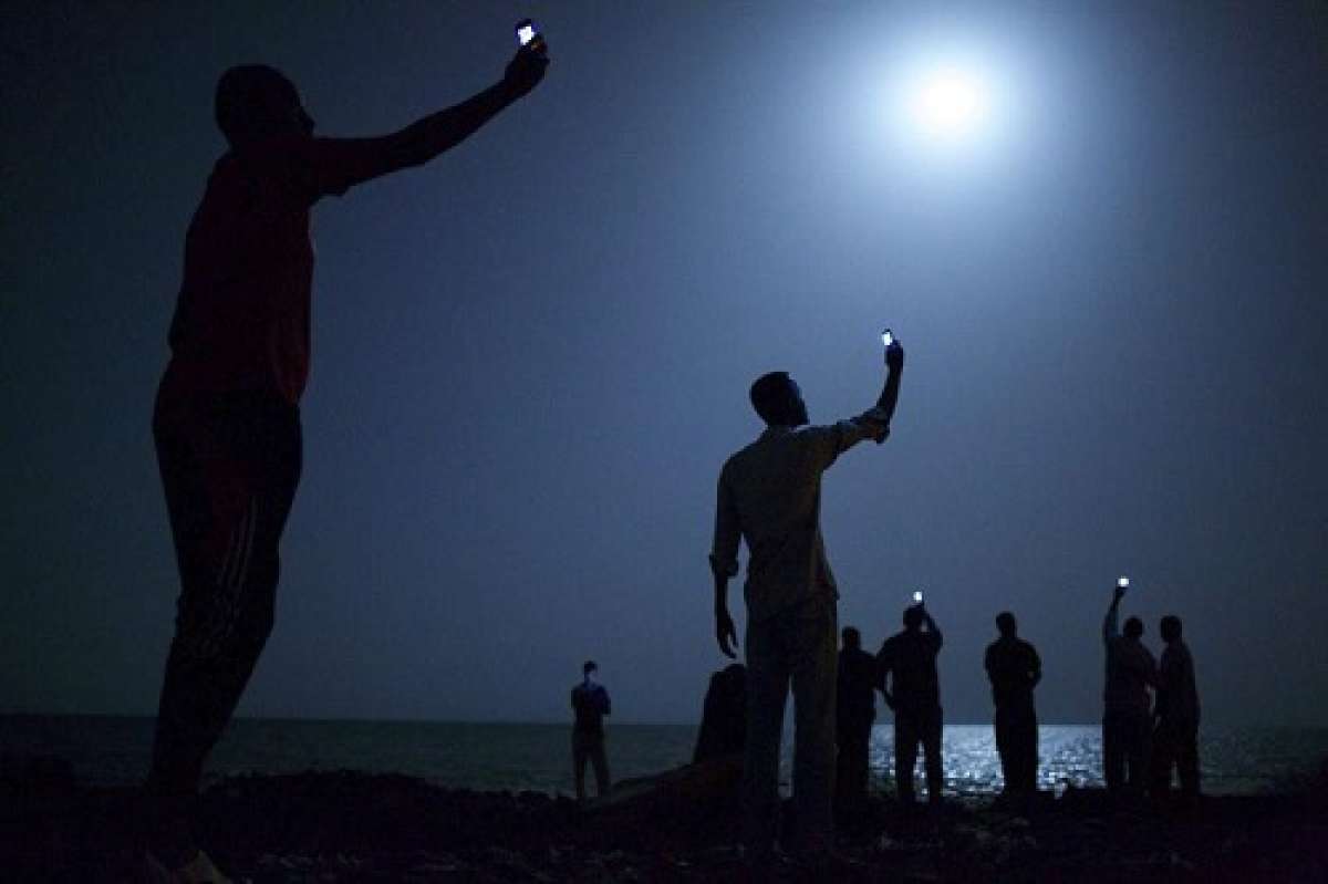 La imagen plasma a un grupo de inmigrantes africanos en Yibuti a la orilla del mar levantando sus tel&eacute;fonos m&oacute;viles para capturar una red telef&oacute;nica de bajo coste de la vecina Somalia. Foto: EFE