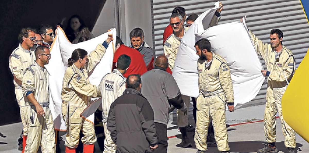 Miembros del equipo de Alonso tapan con telas el traslado del piloto en helic&oacute;ptero hasta el centro de salud. Foto: AFP