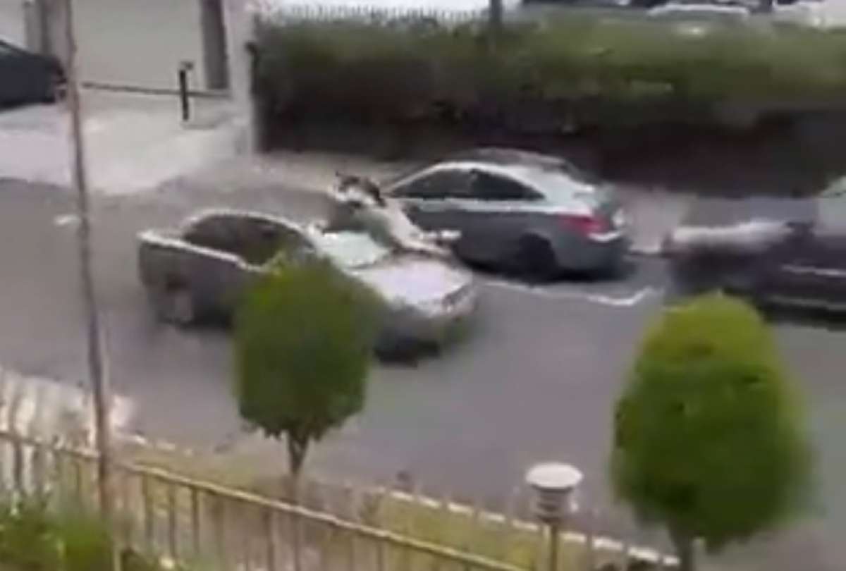 El hombre aferrado al capó de su auto.