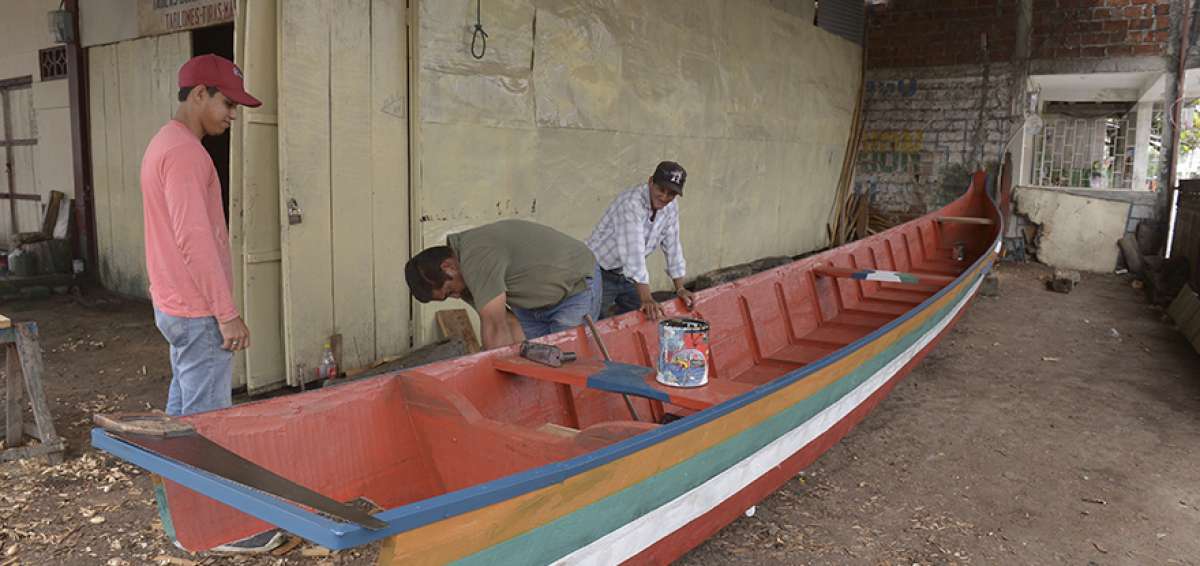 Don Marco da los &uacute;ltimos arreglos a una nueva canoa. Su hijo C&eacute;sar (de pie) lo observa.