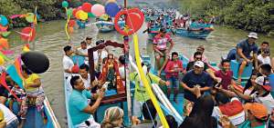 Aproximadamente 60 pangas adornadas con gallardetes y globos parten desde el puerto de San Roque para recorrer el estuario y llegar a La Boca de Crucita. Acompa&ntilde;a a los devotos la banda de pueblo que entona m&uacute;sica religiosa. 