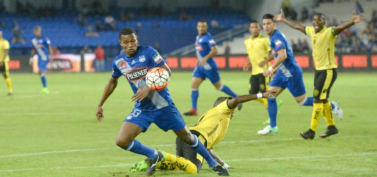  Romario Caicedo (azul) le gana el bal&oacute;n a uno de los defensas de Fuerza Amarilla, que desde el piso reclama al &aacute;rbitro una falta ofensiva del volante azul.