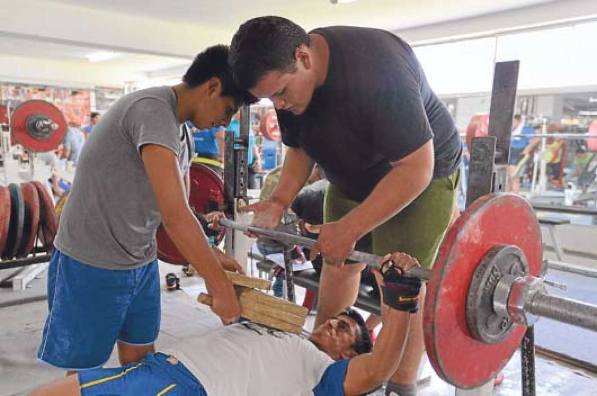 Johnny Chorlango (abajo) se esfuerza para levantar la pesa en el banco, mientras su compa&ntilde;ero Luis Caranqui (derecha) lo asiste. Foto: Miguel Jim&eacute;nez│El tel&eacute;grafo