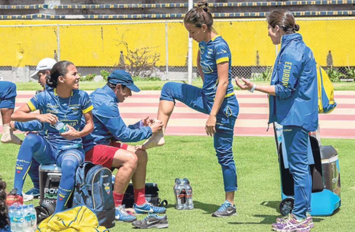 El fisioterapista Hugo Ter&aacute;n (con gorra) venda el pie derecho de la defensa Iliana Bowen durante una pr&aacute;ctica en el estadio Ol&iacute;mpico Atahualpa. Foto: Fernando Sandoval.